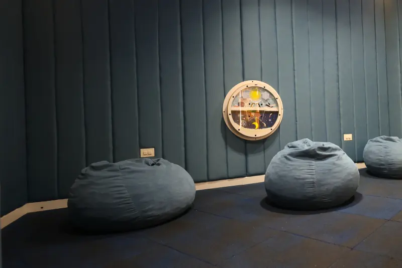 Quiet Room con paredes acolchadas, un panel sensorial redondo y puffs