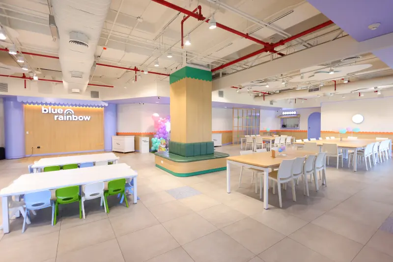 Salón de fiestas con mesas para niños, mesas largas para adultos y el muro con el logotipo de Blue Rainbow