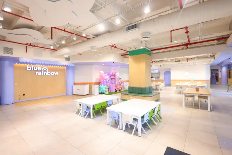 Salón de fiestas con mesas para niños y el muro con el logotipo de Blue Rainbow